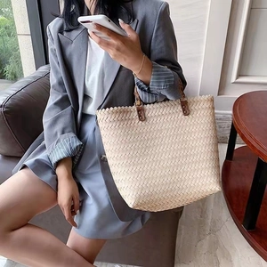 Detailed texture of the beige woven tote bag held by a model in a stylish lifestyle setting