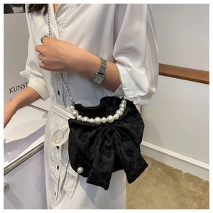 Detail of black bow handbag with white pearl handle and metallic chain strap