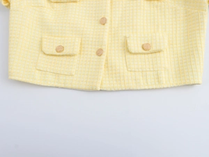Detail of yellow tweed jacket showing texture, metal buttons and flap pocket design