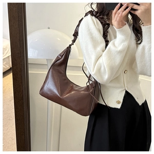 Detail of a brown leather shoulder bag with ruched wide strap and vintage half-moon shape