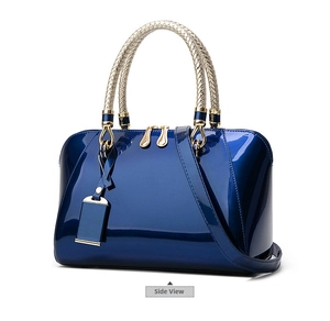 Detail view of glossy navy patent leather handbag with golden woven handle and hardware