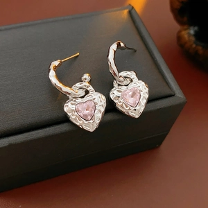 Macro shot of silver C-hoop earrings with textured heart pendant and pink gemstone
