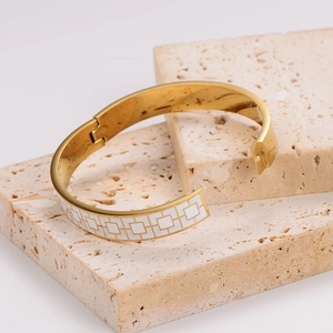 Golden stainless steel bangle with white enamel squares on stone display background