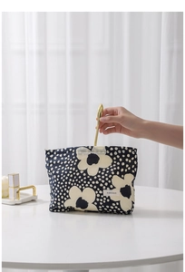 Detail of floral makeup bag featuring hand placing items into dark blue polka dot pouch