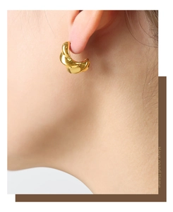 Macro view of gold plated twisted hoop earrings on a model showing high-end texture