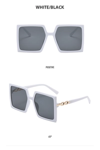 Detail of white square frame sunglasses with golden chain accents and dark lenses