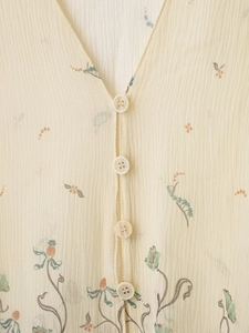 Détail de la blouse en soie beige avec col en V, imprimé floral et boutons blancs