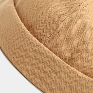 Close-up of brown herringbone weave texture and stitching on a brimless docker hat
