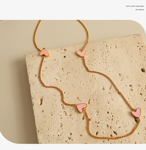 Detailed view of a gold chain necklace with four pink enamel hearts on a stone surface