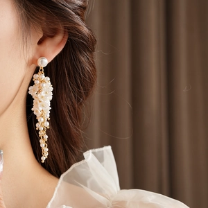 Close-up of floral resin earrings with long elegant pearl tassels worn by a model