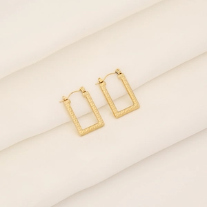 Gold geometric rectangular hoop earrings with Greek key pattern on white textured fabric