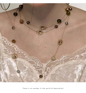 Detail of multi-layer gold chain necklace with colorful gemstone beads on beige lace
