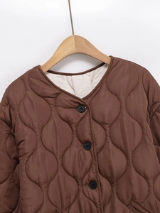 Detail of brown quilted jacket featuring a round neck and contrasting cream lining