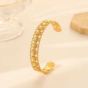 Detail of gold open cuff bracelet with hollowed snowflake pattern in warm lighting