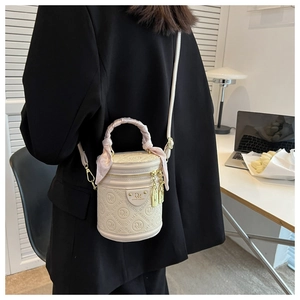 Detail of cream barrel bag with scarf-wrapped handle and golden brand plaque on the front