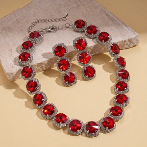 Detail of red ruby style necklace and earrings set with crystal pavé on stone surface