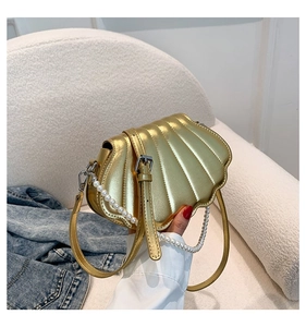 Detail einer goldenen Tasche in Muschelform mit Perlengriff und vertikaler Textur