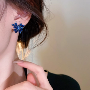 Close-up of elegant butterfly earrings with blue zircons worn by a model in soft light