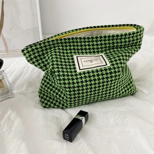 Detail view of woven houndstooth cosmetic bag in green with yellow zipper and brand label