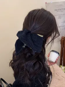 Detail of elegant black jacquard bow hair tie with gold embroidery on curly hair