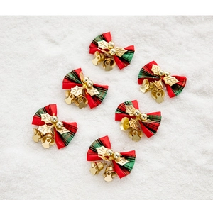 Close-up of six red and green plaid Christmas bows with golden bells and leaves on snow