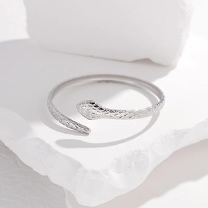 Macro shot of silver snake-patterned C-shaped steel bracelet on a stone pedestal