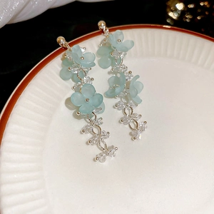 Macro shot of light blue frosted flower tassel earrings with silver chains on a ceramic plate