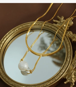Golden double-layer blade chain necklace with textured white pearl pendant on a mirror