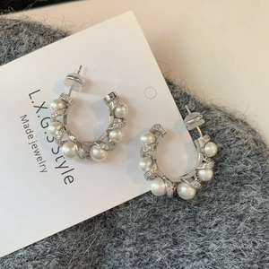 Macro detail of silver C-shape pearl earrings with twisted metal and zircon accents