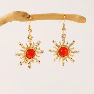 Close-up of golden sun-shaped earrings with red gemstones hanging on a branch