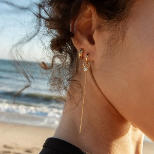 Boucles d'oreilles minimalistes dorées avec pompon et zircon portées par un mannequin