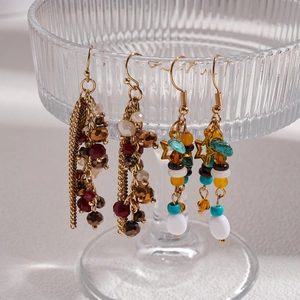 Ethnic fringe earrings with stone beads and star charms hanging on a glass cup rim