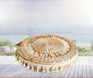 Detail of hand-woven round straw cushion with white fabric center and bohemian tassels