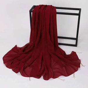 Detail of dark red chiffon shawl with pearl accents and metal tube charms on a rack