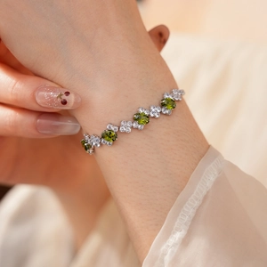 Close-up of a silver zircon bracelet featuring olive green oval stones and white floral gems