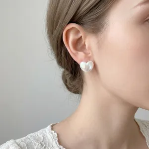 Elegant heart-shaped stud earrings with iridescent pearl finish worn on an ear