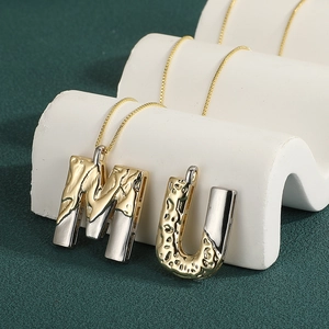 Close-up of dual-tone initial necklaces with molten texture on a white display