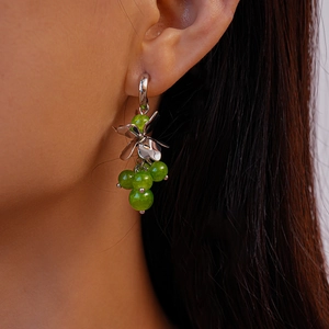 Close-up of C-shaped flower earrings with green glass beads worn on a model ear