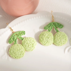 Detailed view of handmade woven cherry earrings in green raffia on a ceramic plate