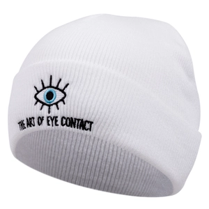 Détail du bonnet blanc en maille côtelée avec broderie d'oeil bleu et texte artistique