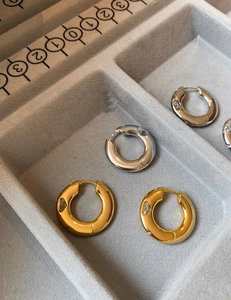 Detail of gold and silver hoop earrings with clear stones on a grey jewelry tray