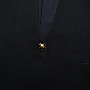 Close-up of a single golden button on a slim fit black blazer with textured fabric
