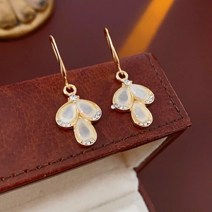 Macro shot of gold leaf earrings with white opal and crystals on a leather jewelry box