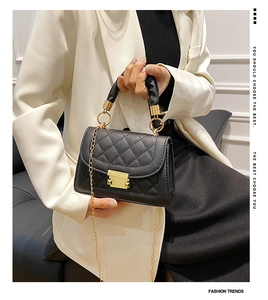 Detalle de bolso negro acolchado con cierre dorado y cadena sobre modelo en traje blanco