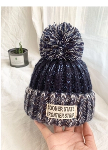 Detail of multi-color knitted beanie with large faux fur pompom and woven label