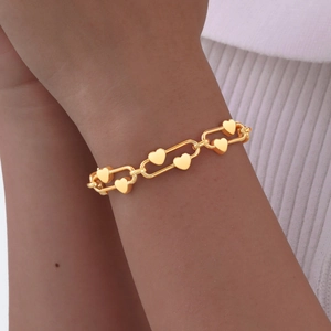 Close-up of golden heart chain bracelet worn on wrist with white knit background