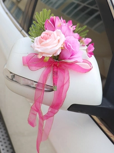 Close-up of pink artificial roses and gold-edged ribbons on a car side mirror