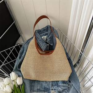 Retro woven straw tote bag with brown leather handles placed on a denim jacket