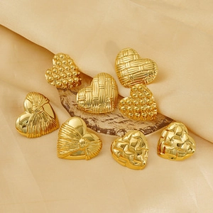 Flat lay of eight gold heart-shaped earrings with embossed textures on silk fabric