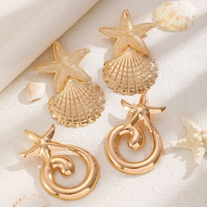 Detail of golden starfish and shell textured earrings on a white beach vacation backdrop